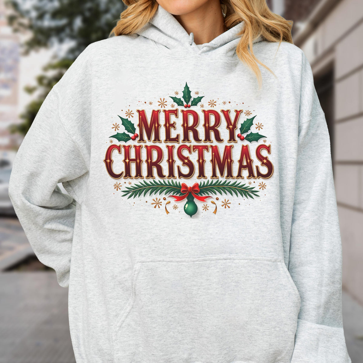 May include: A light gray hoodie featuring a festive "MERRY CHRISTMAS" design in red and brown, adorned with holly leaves, berries, and decorative elements. A red bow and green ornament complete the holiday graphic.