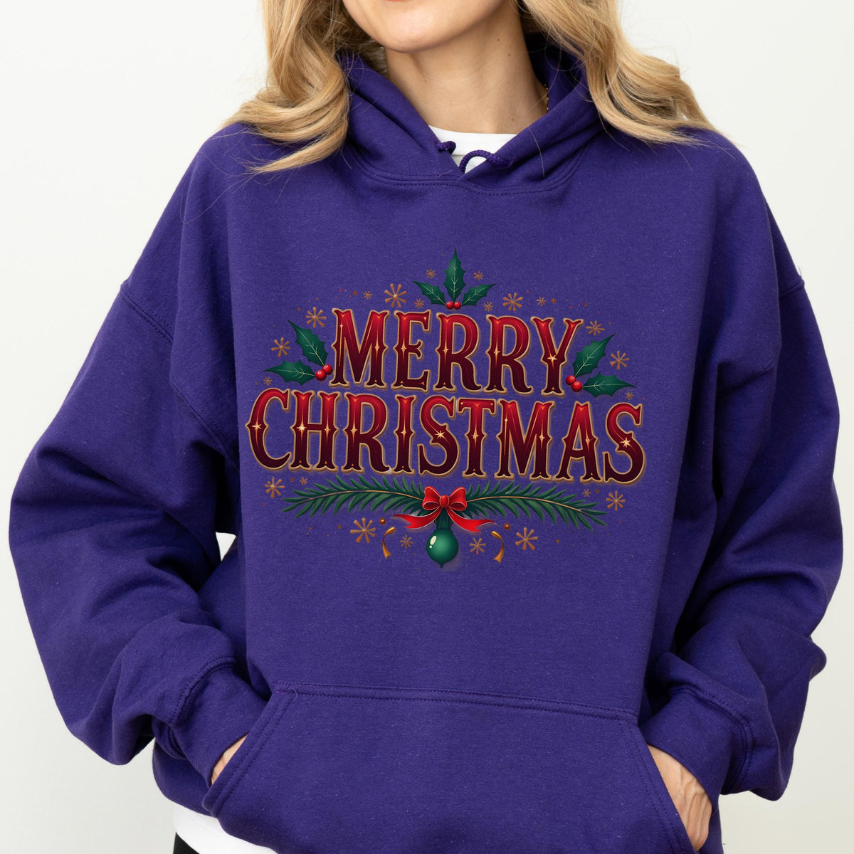 May include: A purple hooded sweatshirt with the words "MERRY CHRISTMAS" in red, outlined in gold. The design includes holly leaves, snowflakes, and a green ornament with a red bow. The sweatshirt has a front pocket.