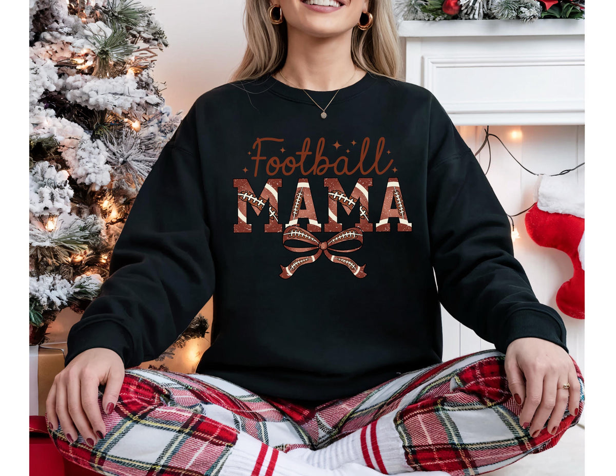 May include: Black sweatshirt with the text "Football MAMA" in brown and white. The word "MAMA" is designed with a football pattern. A brown football bow is below the text. The person is wearing red and white plaid pants.