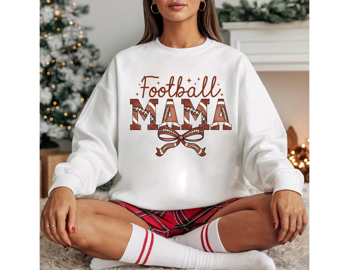 May include: White sweatshirt with the text "Football Mama" in brown and red lettering. The word "Mama" is designed with footballs. A brown bow is below the text. The model is wearing red plaid shorts and white socks with red stripes.