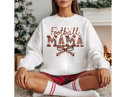 May include: White sweatshirt with the text "Football Mama" in brown and red lettering. The word "Mama" is designed with footballs. A brown bow is below the text. The model is wearing red plaid shorts and white socks with red stripes.