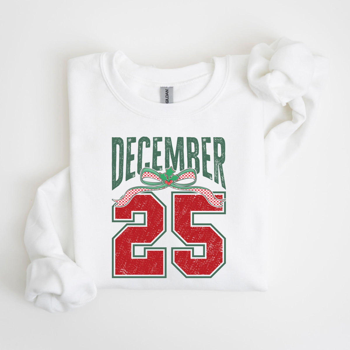 May include: White sweatshirt with the text "DECEMBER 25" in green and red. The text is designed with a distressed, vintage look, and includes a decorative bow with holly leaves.
