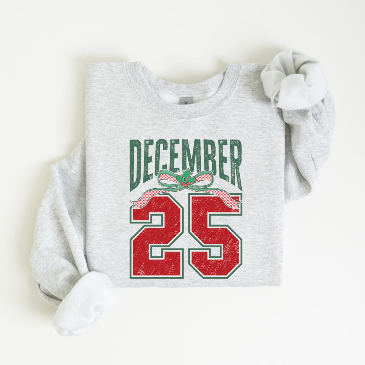 May include: A light gray sweatshirt with the words "DECEMBER 25" printed on the front. The text is in green and red, with a festive bow design. The sweatshirt has long sleeves and a crew neck.