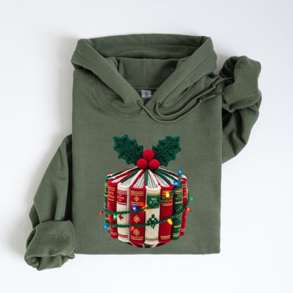 May include: Olive green hoodie with a festive design. The design features a stack of books wrapped with string lights, topped with holly and red berries. The books are red, white, and green, creating a holiday theme.