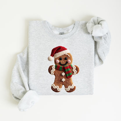 May include: A light gray sweatshirt featuring a gingerbread man graphic. The gingerbread man wears a red Santa hat and a red and green scarf. The graphic is centered on the front of the sweatshirt.