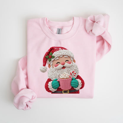 May include: A light pink sweatshirt featuring a festive Santa Claus design. Santa is depicted with a white beard, red hat, and holding a pink mug with whipped cream and a candy cane. The sweatshirt is a solid light pink color.