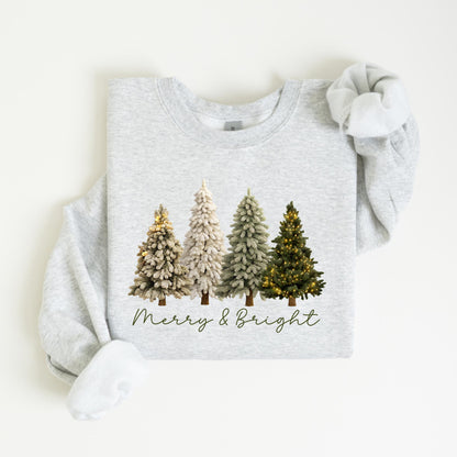 May include: A light gray sweatshirt featuring a graphic of four Christmas trees in varying shades of green and white. The trees are decorated with lights. The words "Merry & Bright" are written in a script font below the trees.