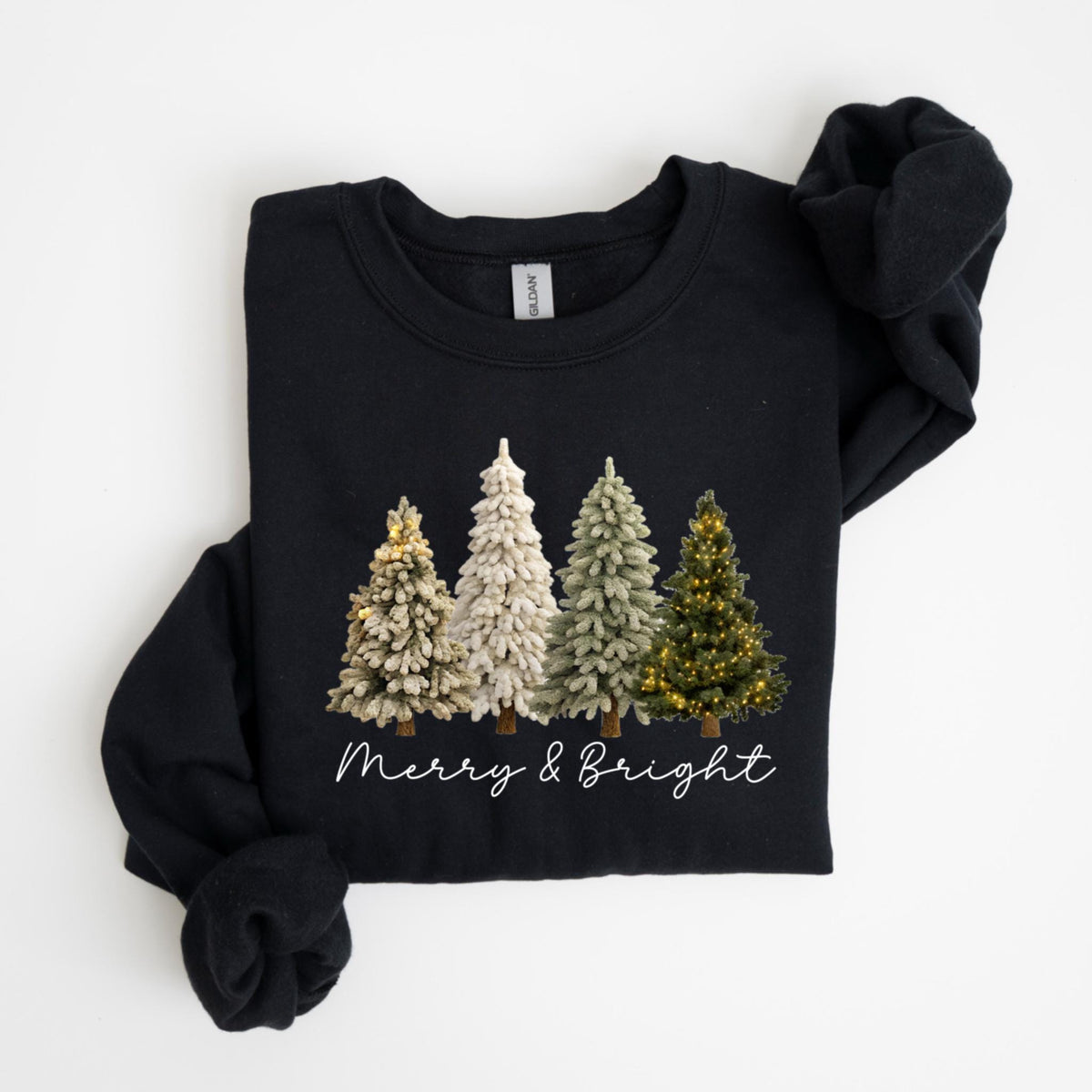 May include: Black sweatshirt featuring a graphic of four Christmas trees in varying shades of green and white. The trees are decorated with lights and sit above the text "Merry & Bright" in a cursive font. The sweatshirt is folded.