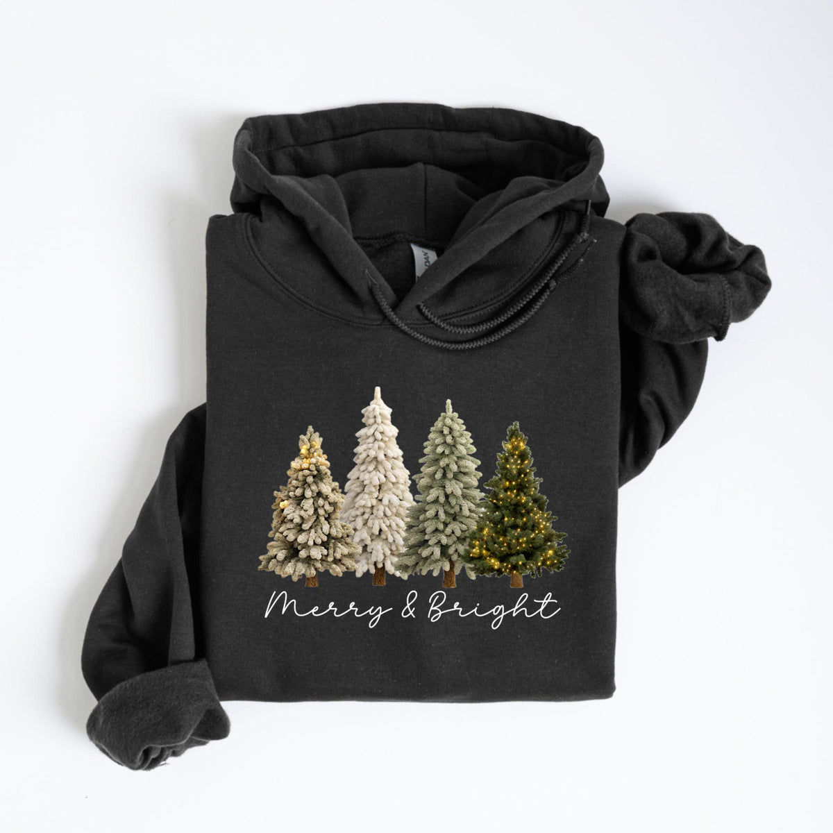 May include: A black hooded sweatshirt featuring a graphic of four Christmas trees in varying shades of white, green, and gold. The text "Merry & Bright" is written in a cursive font below the trees. The sweatshirt is folded on a white surface.