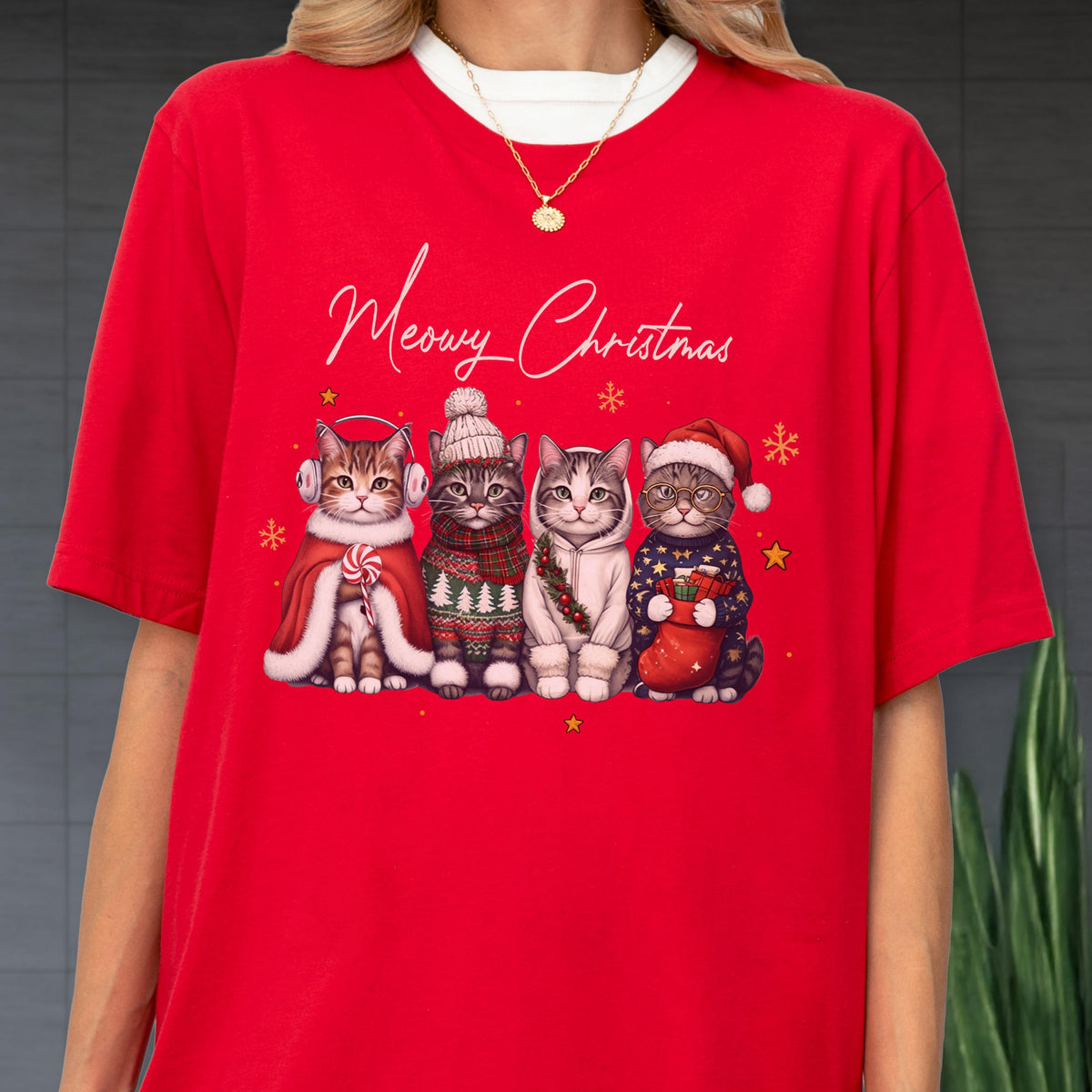 May include: A bright red t-shirt featuring the text Meowy Christmas in white script above a graphic of four cats wearing winter accessories including earmuffs, a knit hat, a scarf, and a Santa hat, surrounded by small yellow stars and snowflakes.