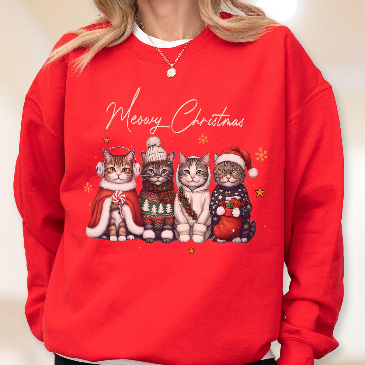 May include: A bright red crewneck sweatshirt featuring the white script text Meowy Christmas above a graphic of four cats. The cats are wearing winter accessories including earmuffs, a knit hat, a scarf, a hoodie, and a Santa hat with a stocking.