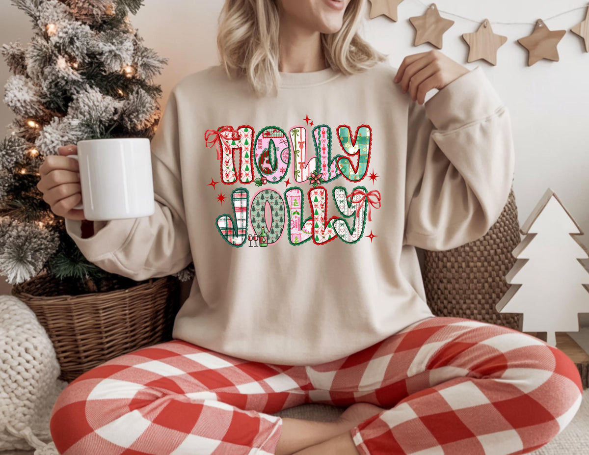May include: A beige sweatshirt with the words "HOLLY JOLLY" in a colorful, festive design. The letters are decorated with plaid, Christmas trees, and bows. The person is wearing red and white plaid pajama pants and holding a white mug.