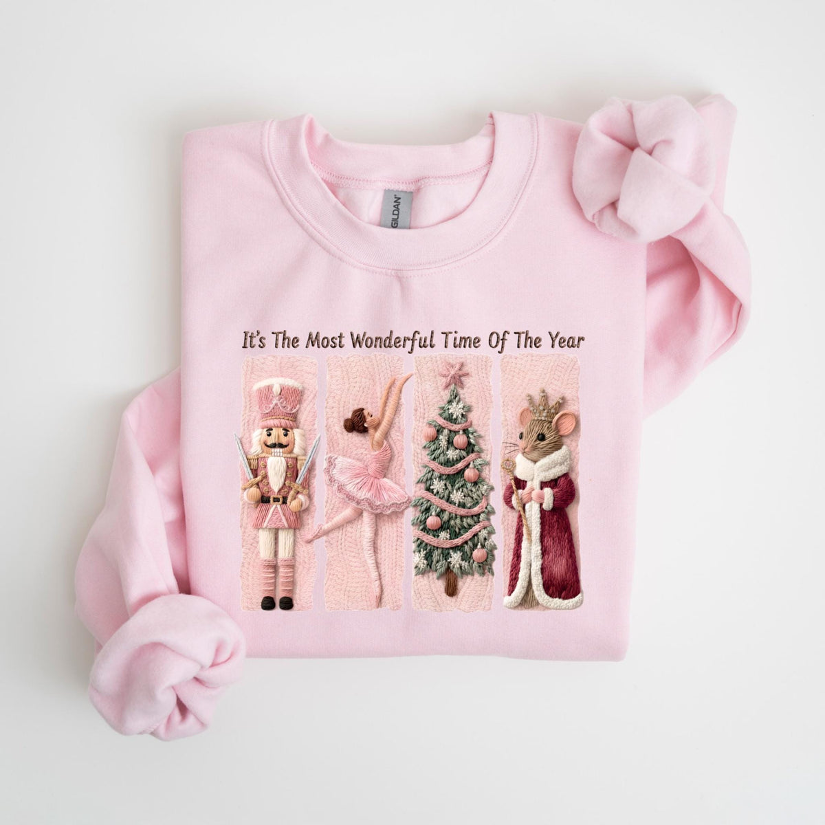 May include: A light pink sweatshirt featuring a festive design with a nutcracker, ballerina, Christmas tree, and mouse king. The text "It's The Most Wonderful Time Of The Year" is printed above the illustrations. The sweatshirt has long sleeves and a crew neck.