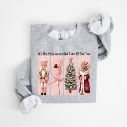 May include: A light gray sweatshirt with the text "It's The Most Wonderful Time Of The Year." The graphic features a nutcracker, a ballerina, a Christmas tree, and a mouse in a red coat. The design has pink and white accents.
