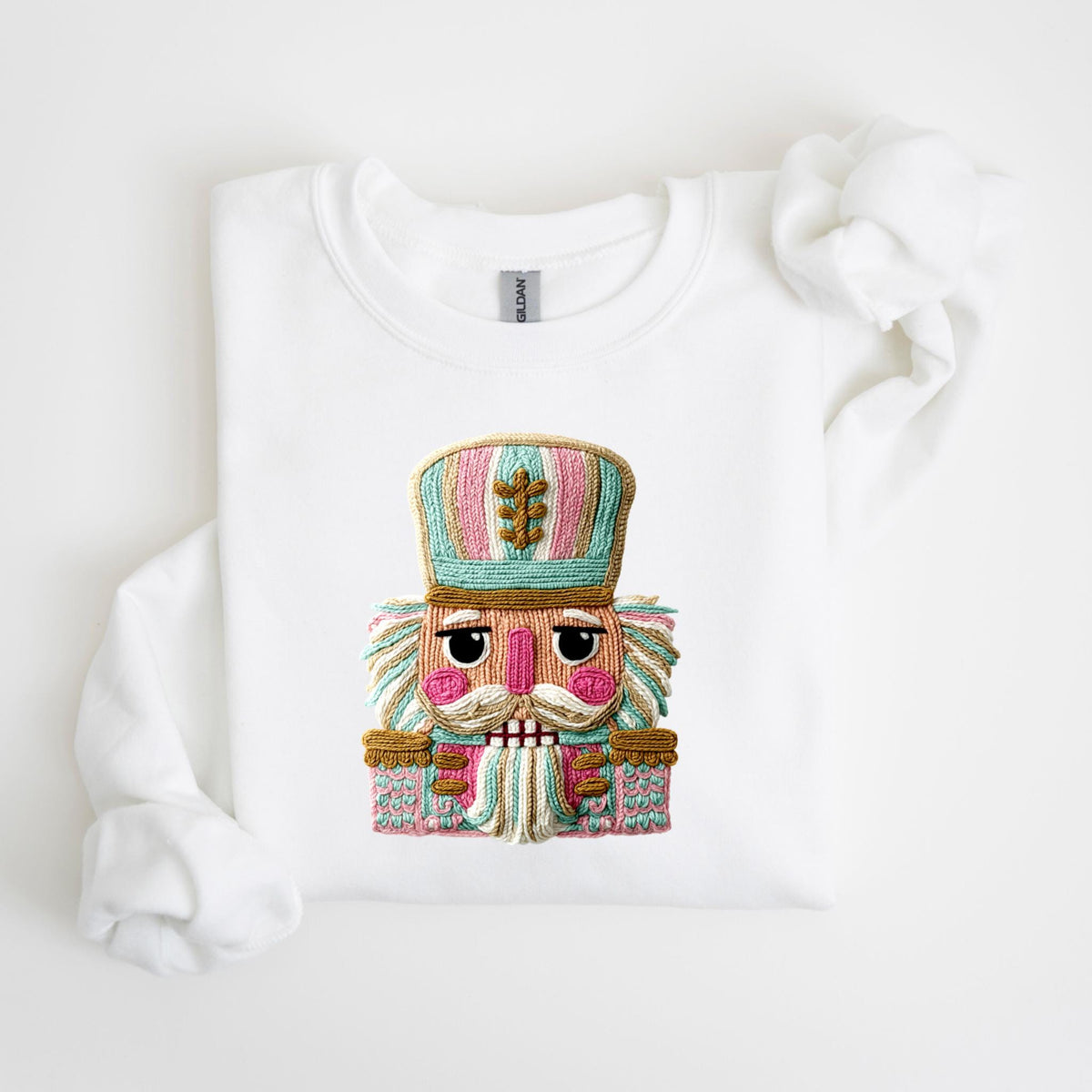 May include: White sweatshirt featuring a colorful embroidered nutcracker design. The nutcracker has a pink, blue, and gold color scheme, with a detailed face and hat. The design is centered on the front of the sweatshirt.