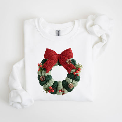 May include: White sweatshirt featuring a knitted Christmas wreath design. The wreath is composed of green and light green knitted sections, adorned with a red bow, pinecones, and red berries. The sweatshirt has a crew neck and long sleeves.
