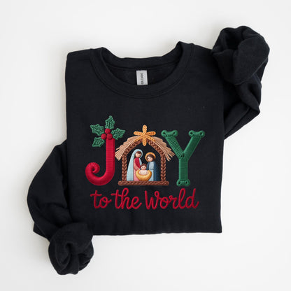 May include: Black sweatshirt with embroidered text and design. The design includes the word "JOY" with a nativity scene and the phrase "to the World" in red thread. The letter "J" is red with holly, the "Y" is green, and the nativity scene is in a wooden stable.
