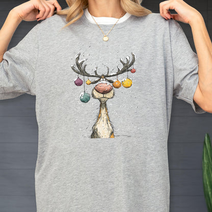 May include: A light gray t-shirt featuring a whimsical cartoon reindeer with colorful ornaments hanging from its antlers. The reindeer has a large pink nose and a long neck. The design is a festive, winter-themed graphic.