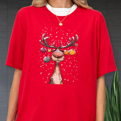 May include: Red t-shirt featuring a whimsical cartoon reindeer with large antlers and colorful ornaments. The reindeer has a large, red nose and is set against a snowy background. The shirt has a white crew neck.