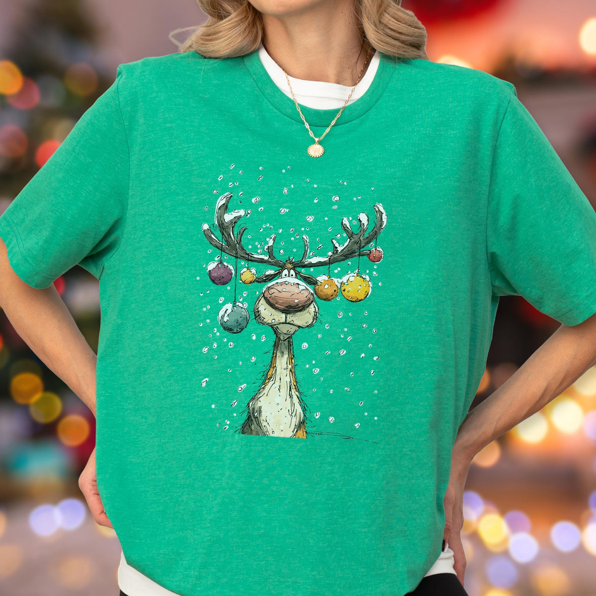 May include: Green t-shirt featuring a cartoon reindeer with large antlers decorated with colorful ornaments. The reindeer is depicted in a snowy scene. The shirt is a crew neck and has short sleeves. Christmas-themed apparel.
