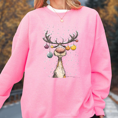 May include: A bright pink long-sleeve sweatshirt featuring a central graphic illustration of a reindeer with large antlers decorated with colorful hanging ornaments. The reindeer has a prominent nose and is surrounded by small white dots resembling snow.
