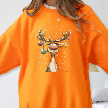 May include: A bright orange crewneck sweatshirt featuring a central graphic illustration of a reindeer with large antlers decorated with colorful hanging ornaments, set against a background of falling white snow dots and a light dusting of snow.