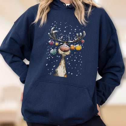 May include: A navy blue hooded sweatshirt featuring a graphic print of a reindeer with large antlers decorated with colorful hanging ornaments. The reindeer is depicted against a backdrop of falling white snowflakes, with a large front pocket.