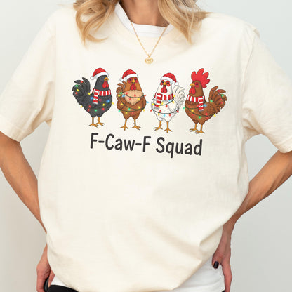 May include: Cream-colored t-shirt featuring a graphic of four cartoon roosters wearing Santa hats and Christmas lights. The text "F-Caw-F Squad" is printed below the roosters. The shirt is made of a soft material.