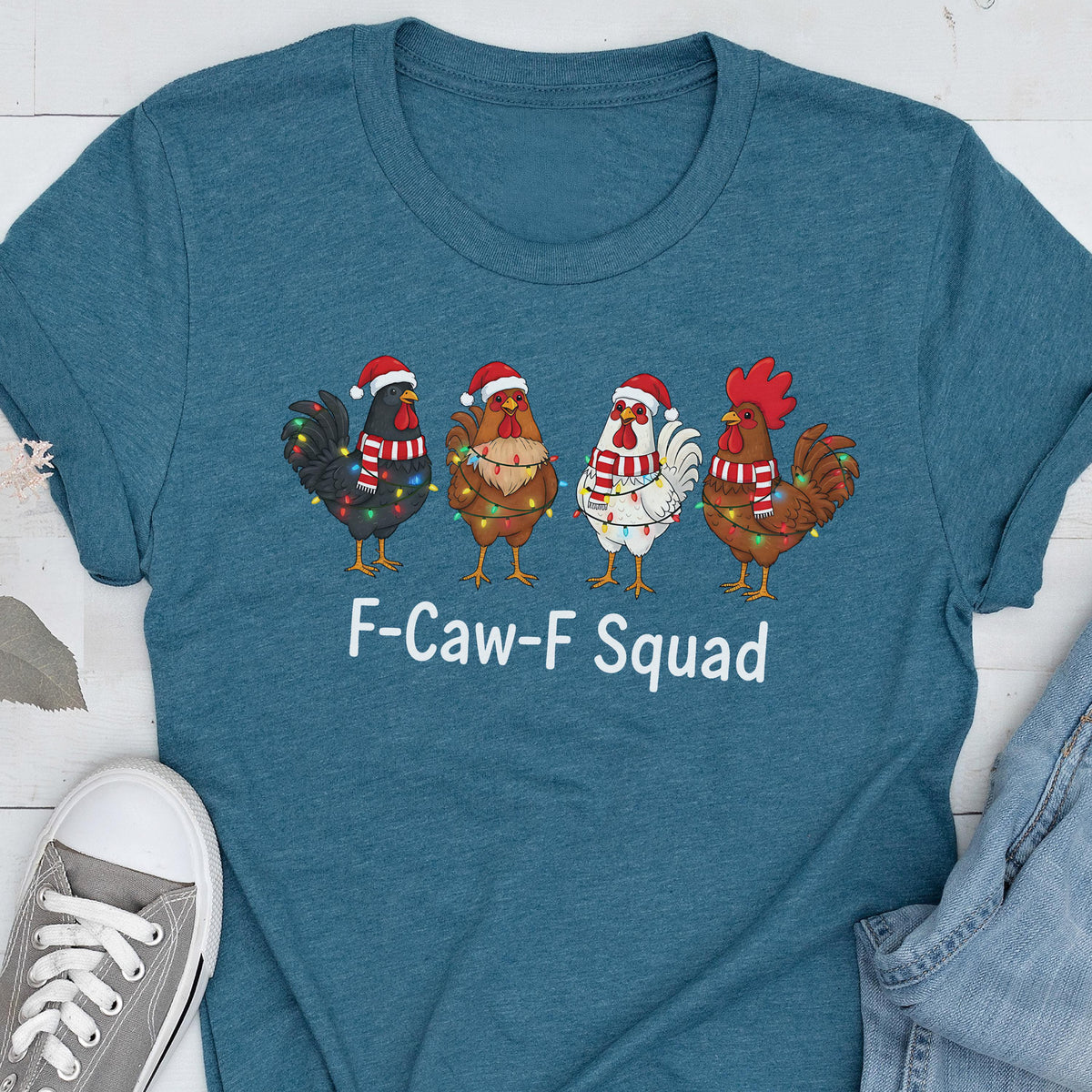 May include: Teal t-shirt featuring a graphic of four cartoon chickens wearing Santa hats and Christmas lights. The text "F-Caw-F Squad" is printed below the chickens in white. The shirt is made of a soft material.