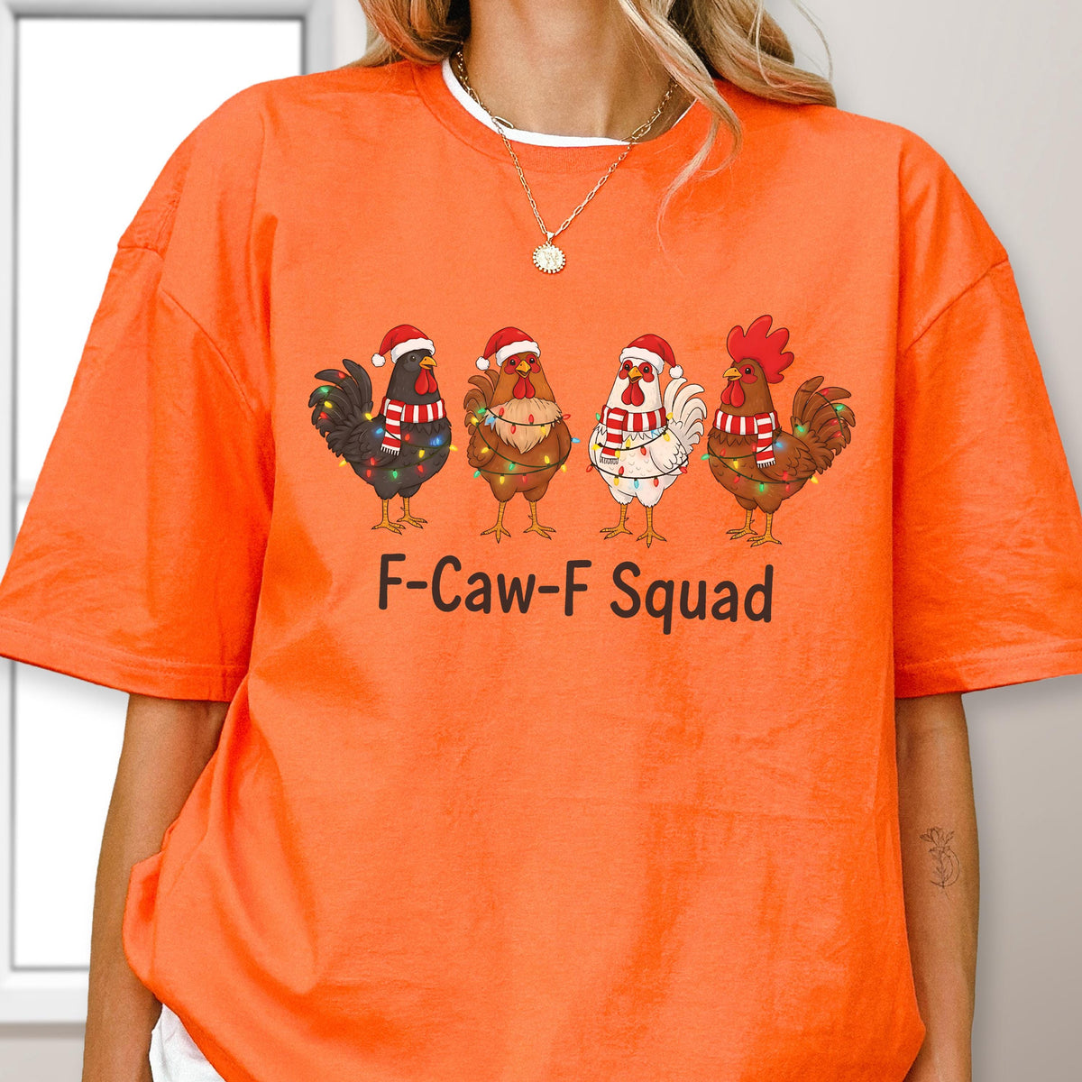 May include: Orange t-shirt featuring a graphic of four cartoon roosters wearing Santa hats and scarves, adorned with Christmas lights. The text "F-Caw-F Squad" is printed below the roosters. The shirt has short sleeves and a crew neck.