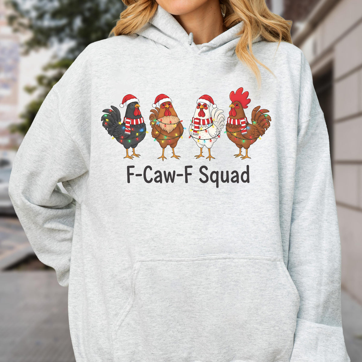 May include: A light gray hoodie featuring a festive design. The graphic shows four chickens, each adorned with Santa hats, scarves, and string lights. The text "F-Caw-F Squad" is printed below the chickens.