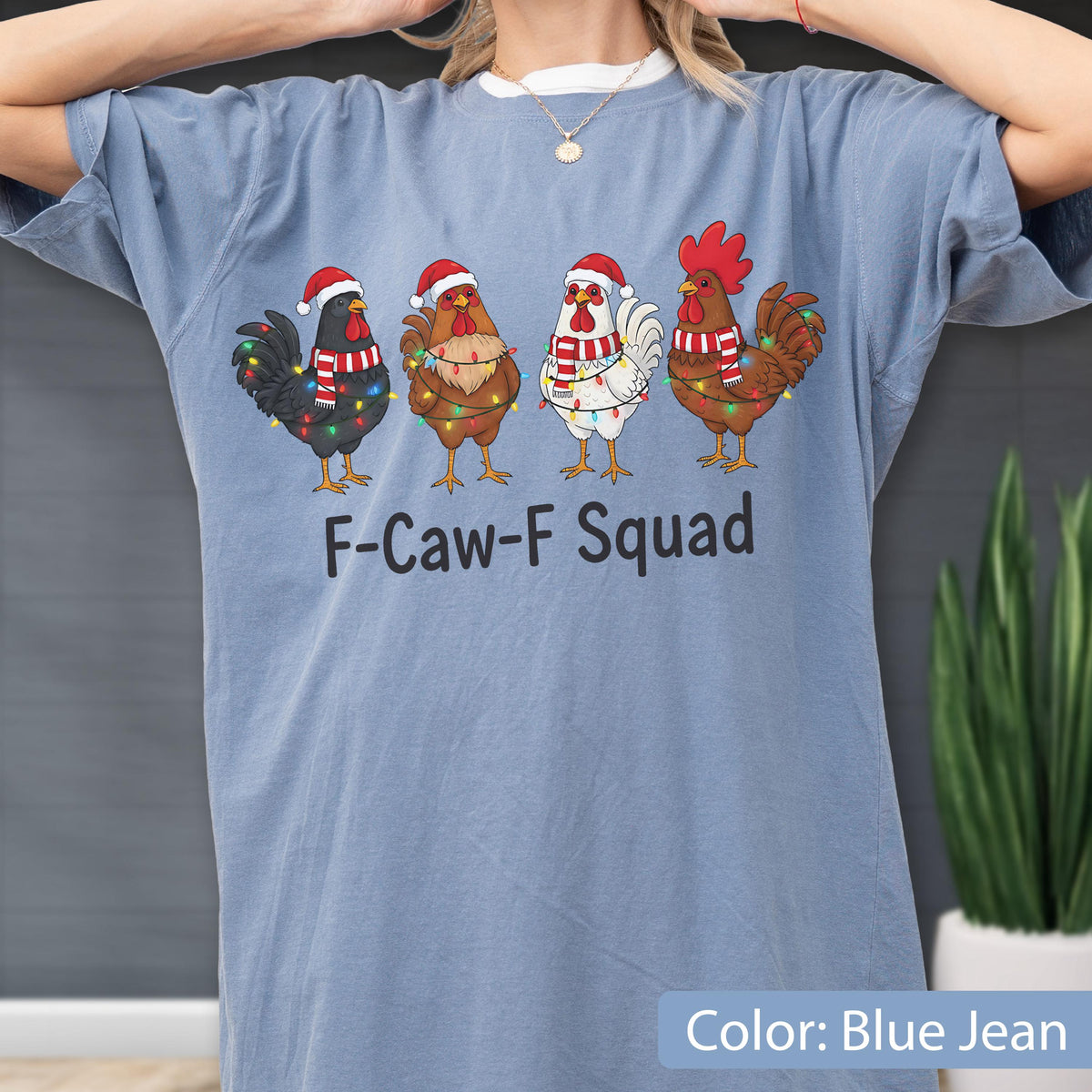 May include: Blue jean colored t-shirt featuring a graphic of four chickens wearing Santa hats and Christmas lights. The text "F-Caw-F Squad" is printed below the chickens. The shirt is a comfortable, casual style.