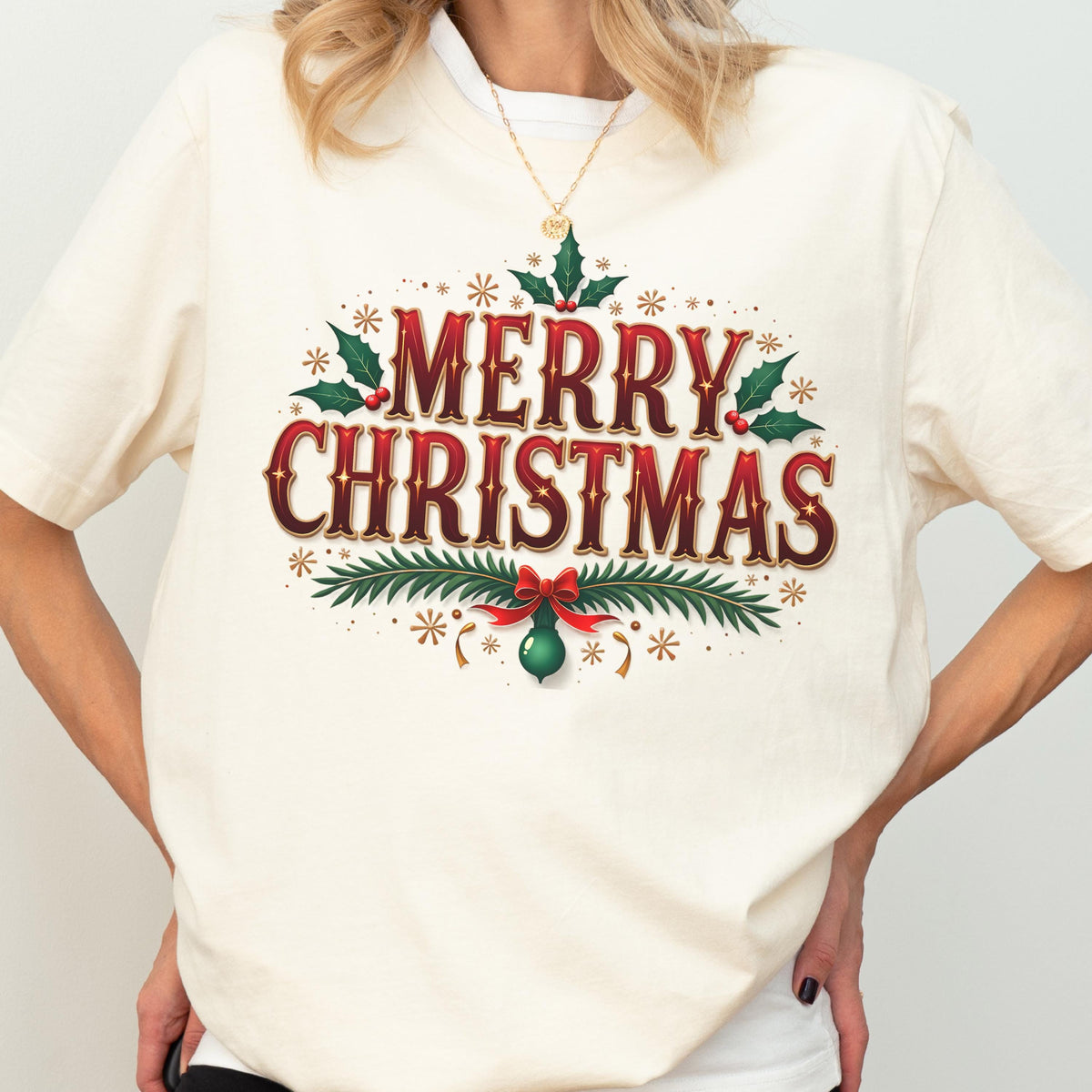 May include: A cream-colored t-shirt featuring the text Merry Christmas in a bold red font with a dark outline. The design includes green holly leaves with red berries, pine branches, a red bow, and a green ornament, accented by small gold stars.