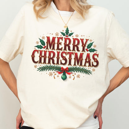 May include: A cream-colored t-shirt featuring the text Merry Christmas in a bold red font with a dark outline. The design includes green holly leaves with red berries, pine branches, a red bow, and a green ornament, accented by small gold stars.