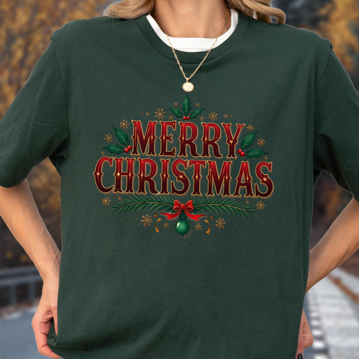 May include: A dark green crew neck t-shirt featuring the red and gold text Merry Christmas in a decorative font. The design includes green holly leaves with red berries, pine branches, a red bow, and small gold star accents centered on the chest.