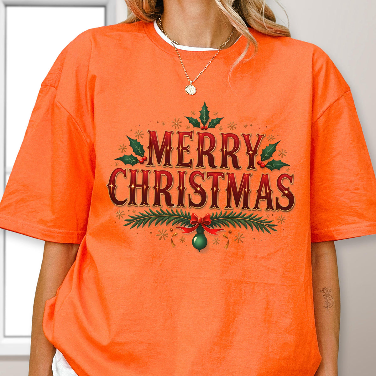 May include: A bright orange short-sleeve t-shirt featuring the text MERRY CHRISTMAS in a dark red font. The design is decorated with green holly leaves, red berries, and a green ornament hanging from a red bow, surrounded by small gold stars.