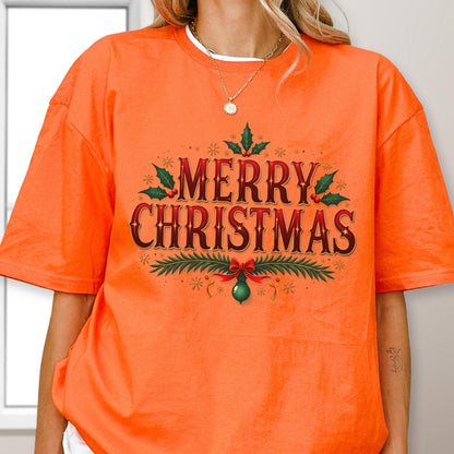 May include: A bright orange short-sleeve t-shirt featuring the text MERRY CHRISTMAS in a dark red font. The design is decorated with green holly leaves, red berries, and a green ornament hanging from a red bow, surrounded by small gold stars.