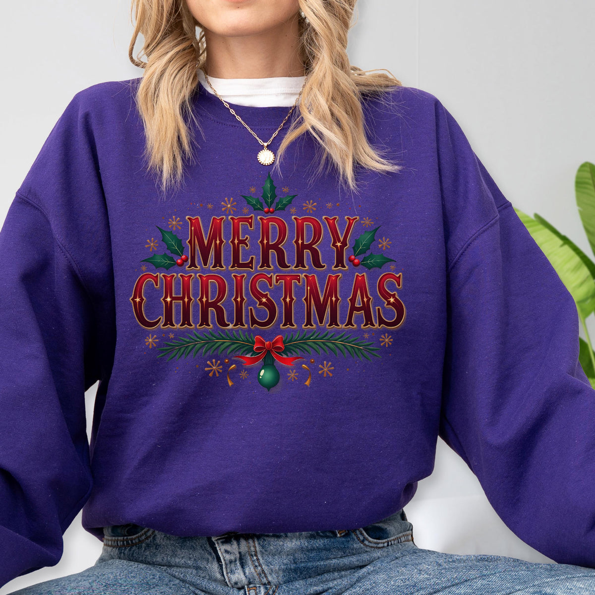 May include: A purple sweatshirt with the words "MERRY CHRISTMAS" in a decorative font. The text is surrounded by holly leaves, berries, and snowflakes. A red bow and a green ornament are at the bottom of the design.