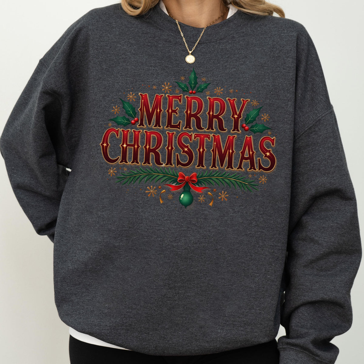 May include: A dark gray sweatshirt featuring a festive "MERRY CHRISTMAS" design in red and gold. The design includes holly leaves, berries, snowflakes, and a green ornament with a red bow, perfect for the holiday season.