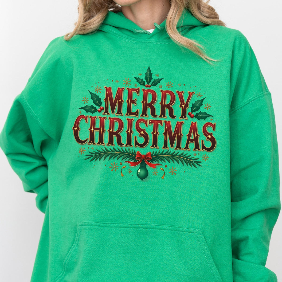 May include: A green hooded sweatshirt with the words "MERRY CHRISTMAS" in a festive design. The text is in red with a brown outline, adorned with holly leaves, snowflakes, and a red bow with a green ornament. The sweatshirt is a solid green color.