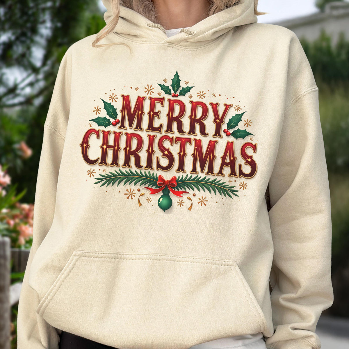 May include: Cream-colored hoodie with a festive "MERRY CHRISTMAS" graphic in red and green. The design includes holly leaves, berries, and a decorative bow. The hoodie has a front pocket and a hood.