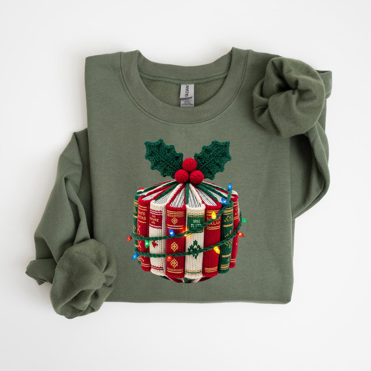 May include: Olive green sweatshirt with a festive design. The design features a stack of books decorated with holly leaves, red berries, and a string of colorful Christmas lights. The sweatshirt has long sleeves and a crew neck.