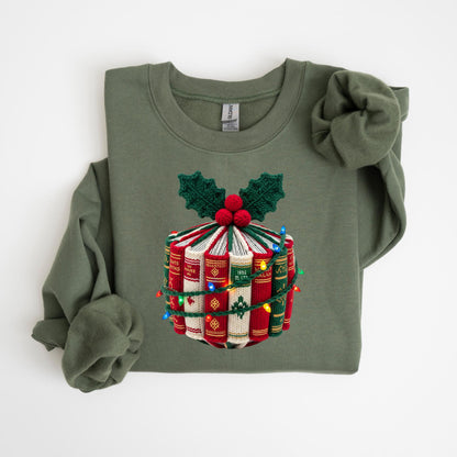 May include: Olive green sweatshirt with a festive design. The design features a stack of books decorated with holly leaves, red berries, and a string of colorful Christmas lights. The sweatshirt has long sleeves and a crew neck.