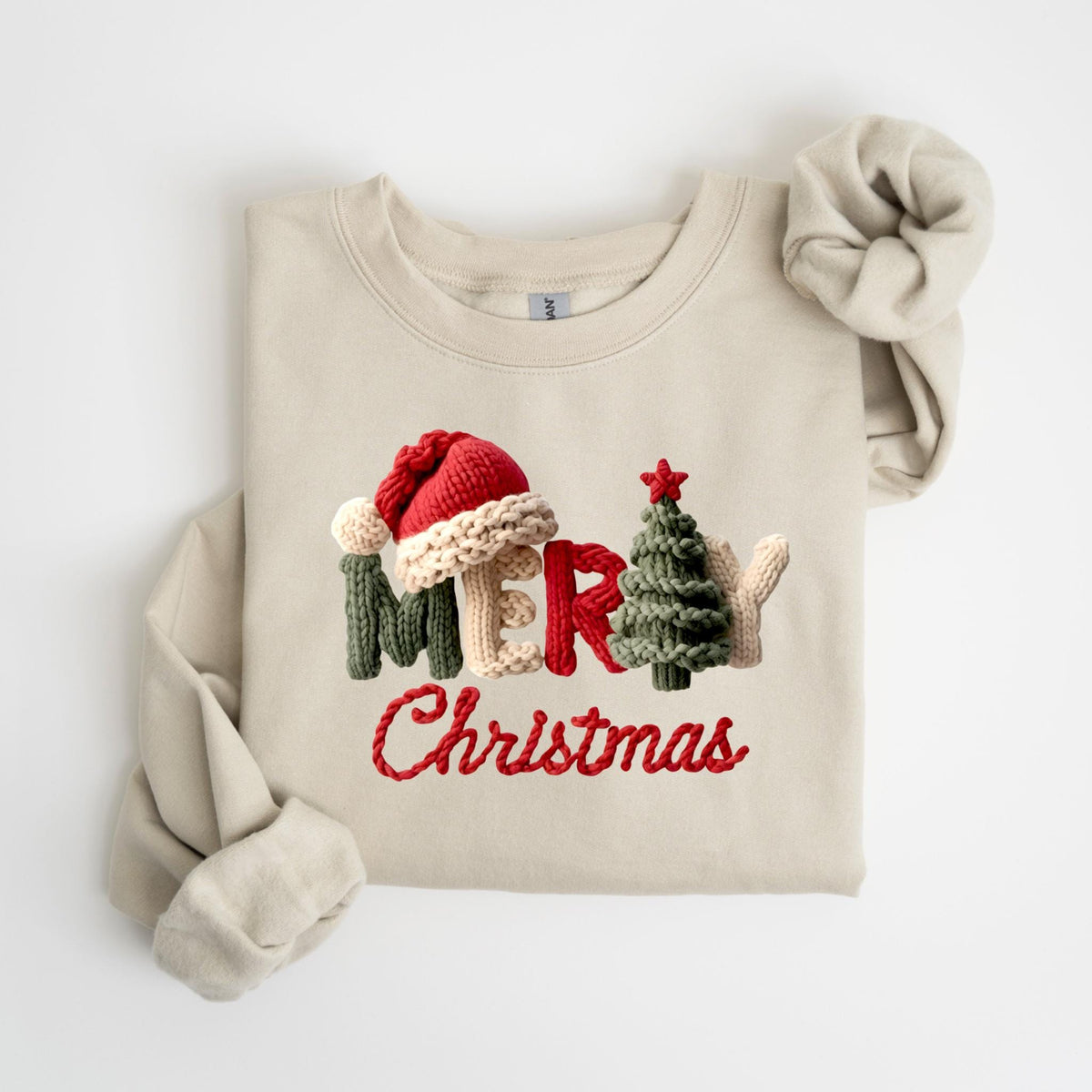 May include: A beige sweatshirt with the words "MERRY Christmas" in a knitted design. The word "MERRY" features a Santa hat, a Christmas tree, and a mitten. The text is in red and green.
