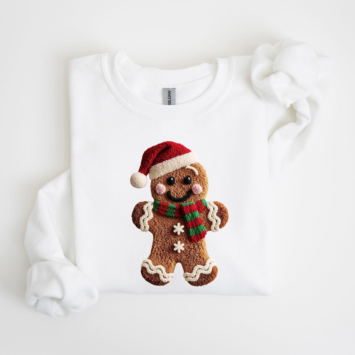 May include: White sweatshirt featuring a gingerbread man design. The gingerbread man wears a red and white Santa hat and a green and red scarf. The gingerbread man has a smiling face and two white snowflakes.