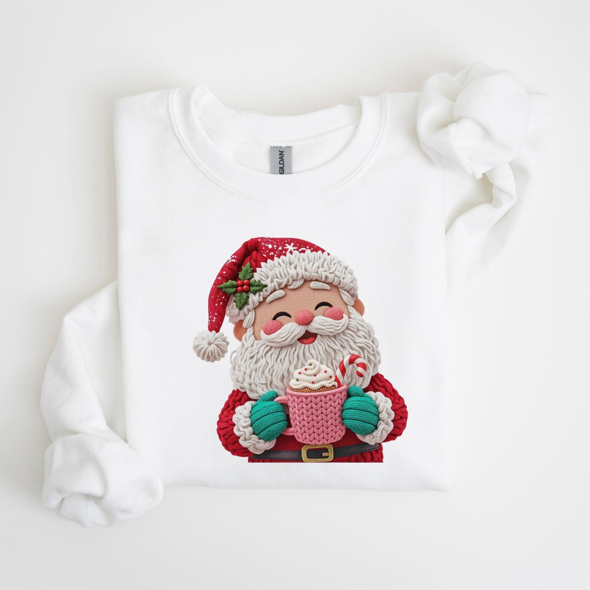 May include: White sweatshirt featuring a festive Santa Claus design. Santa is depicted with a red hat, white beard, and holding a pink mug with whipped cream and a candy cane. The design includes green gloves and a brown belt.