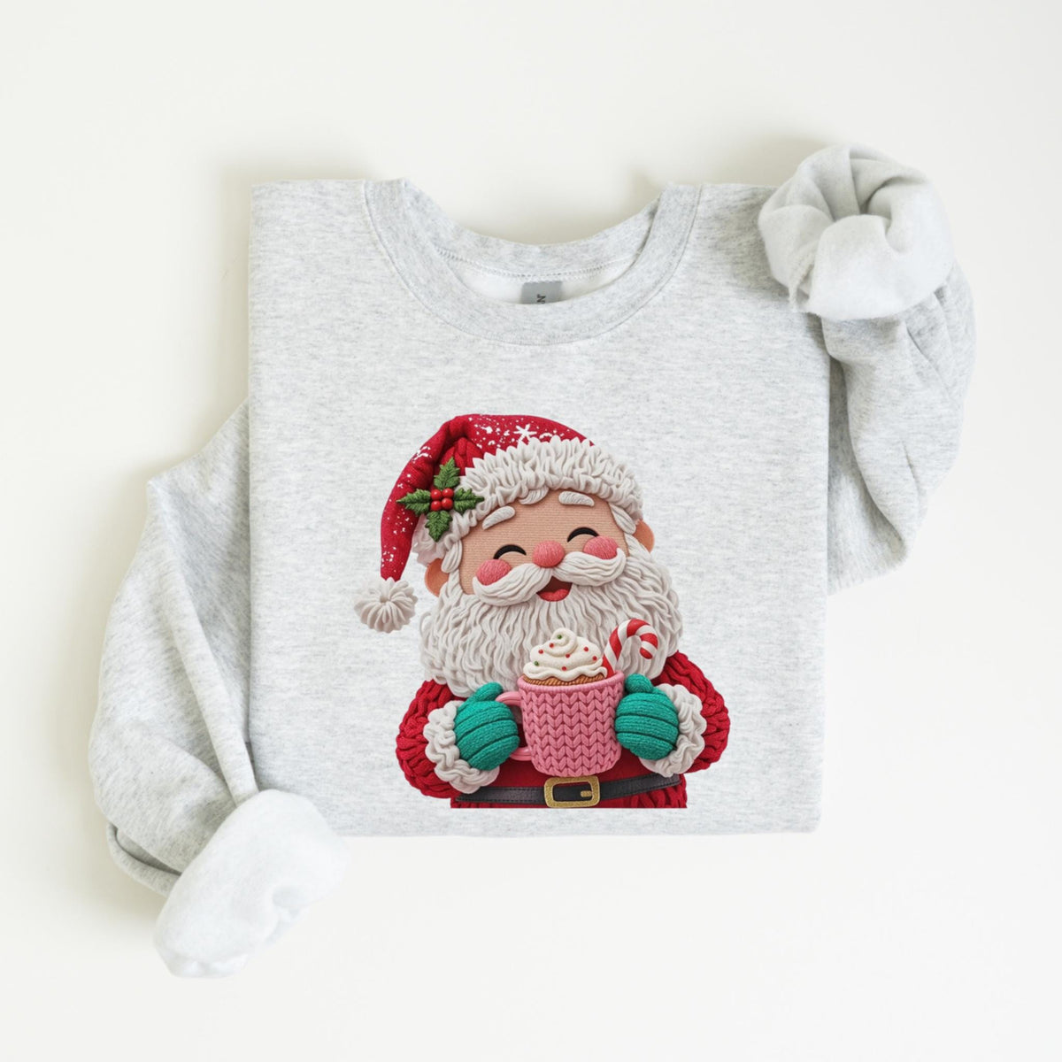 May include: A light gray sweatshirt featuring a festive Santa Claus design. Santa is depicted with a red hat, white beard, and holding a pink mug with whipped cream and a candy cane. The design is in a 3D style.