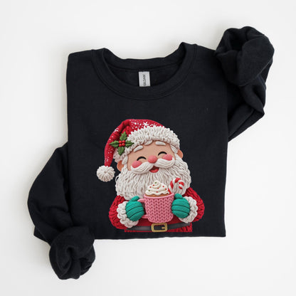 May include: Black sweatshirt featuring a colorful Santa Claus graphic. Santa is depicted with a white beard, red suit, and a hat with holly. He holds a pink mug with whipped cream and a candy cane. The sweatshirt is folded.