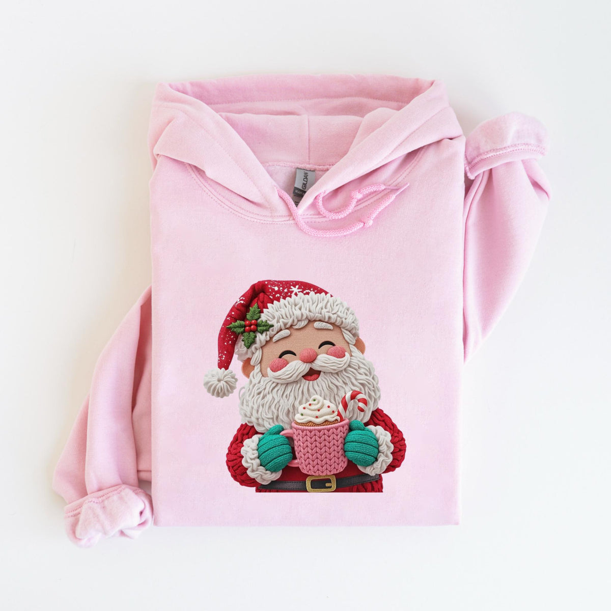 May include: A light pink hoodie featuring a Santa Claus graphic. The Santa illustration shows a smiling face, a red hat, and a white beard, holding a pink mug with whipped cream and a candy cane. The hoodie has a drawstring hood and long sleeves.