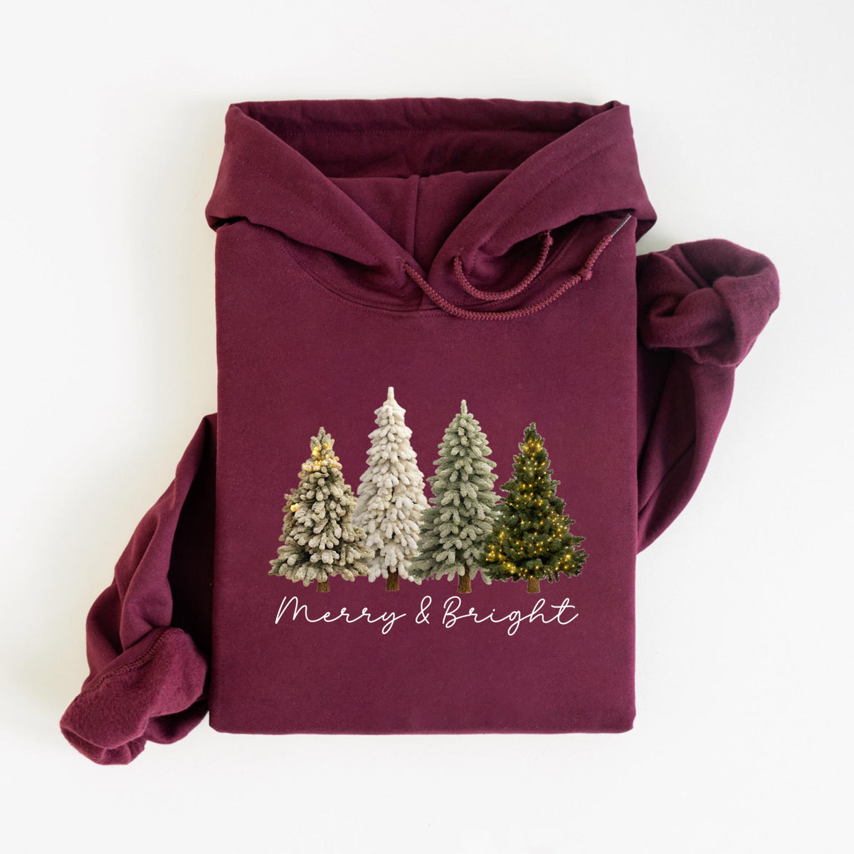 May include: A maroon hoodie featuring a festive design. The graphic includes four stylized Christmas trees in varying shades of green and white, with one tree adorned with yellow lights. The words "Merry & Bright" are written in a cursive font below the trees.